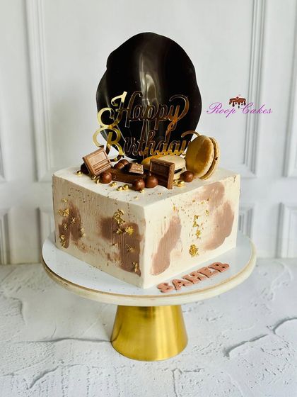 Chic, classy, and irresistibly delicious. This modern square cake features a glossy chocolate sail, gold leaf accents, and indulgent chocolate treats.