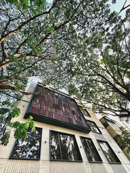 An upward view of our mixed-use project, where we integrated a distinctive wooden screen facade with the surrounding natural canopy. This approach softens the modern structure and creates a harmonious blend of architecture and nature.