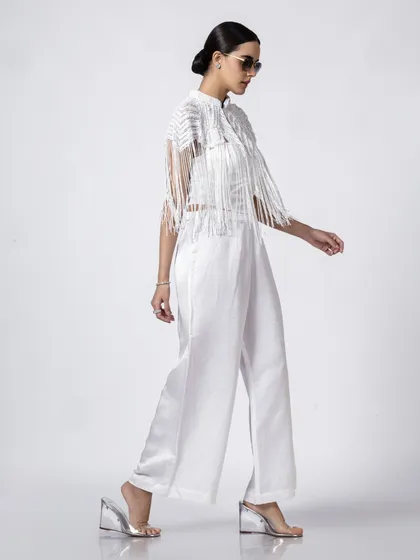 A model walks in a white outfit with fringe details. The clean studio background and full-length shot are perfect for clearly showcasing the garment's design and movement for an e-commerce catalogue.