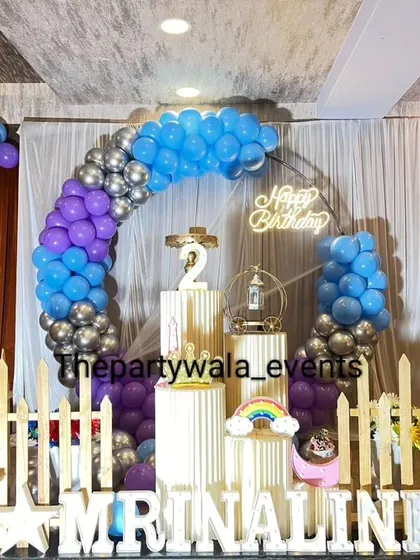A purple, blue, and silver balloon arch against a white curtain. This color combination is cool and modern, perfect for a stylish birthday party.