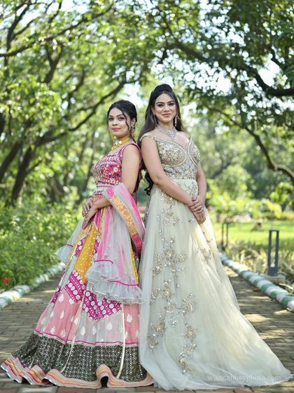 A back-to-back pose highlighting a colorful sangeet lehenga and a sophisticated reception gown. Both outfits are available for rent with matching jewellery.