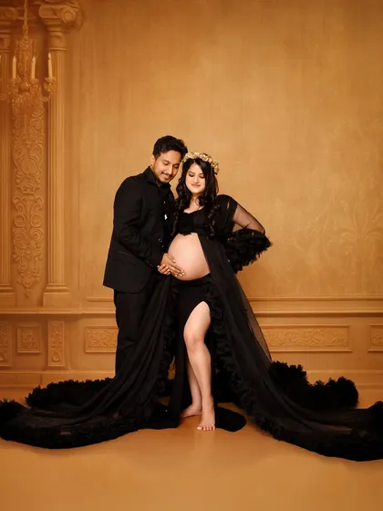 An elegant couple's maternity portrait using a classic painted backdrop. The couple is dressed in formal black, creating a sophisticated and timeless look that focuses on their connection and anticipation.