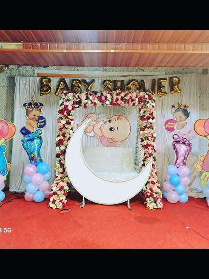 A classic baby shower setup with a floral swing, lighted moon, and 'It's a Boy'/'It's a Girl' props, suitable for any home or small venue.