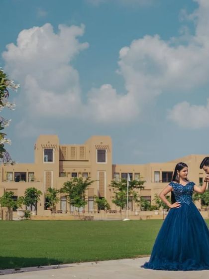 A classic romantic pose with the groom kissing his partner's hand, showcasing the full silhouette of the navy blue ball gown against a beautiful backdrop.