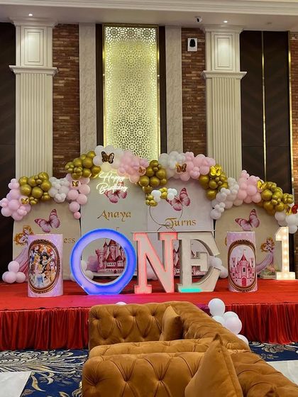 A grand princess-themed stage for a first birthday celebration. This setup includes multiple backdrops, balloon arrangements, and large letters spelling 'ONE'.