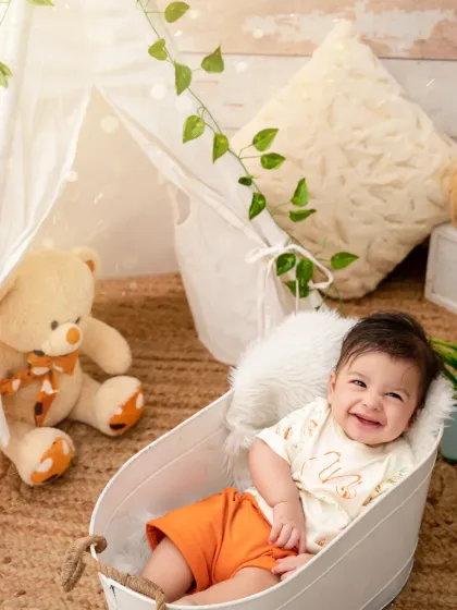 Our little camper is stealing hearts with his radiant smile, relaxing in a cozy tent setup with his teddy bear.