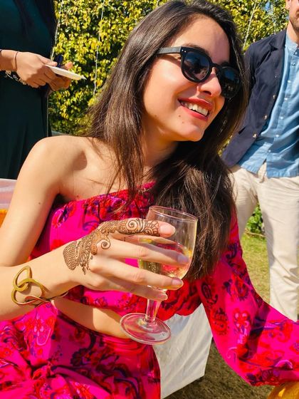 A happy, smiling client enjoying a drink at a party, with her chic finger henna on display.