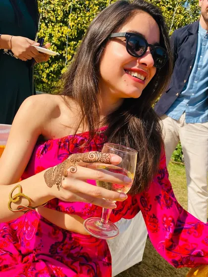 A happy, smiling client enjoying a drink at a party, with her chic finger henna on display.