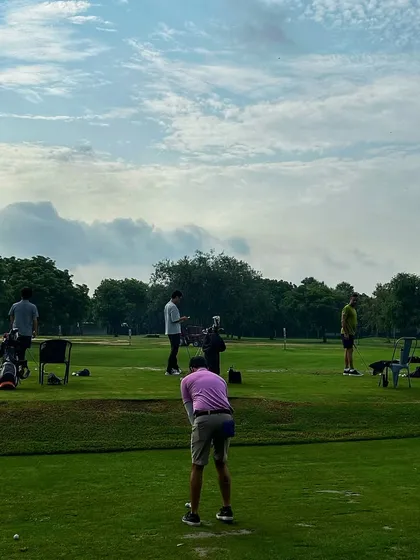 A golfer in a pink shirt stands out against the green, focused on his shot on a busy Saturday.