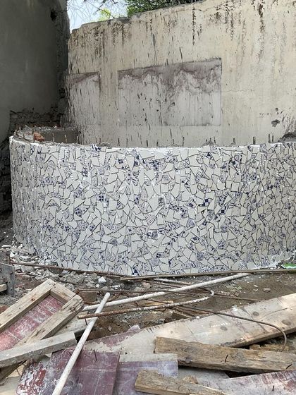A work-in-progress shot of a curved seating element being finished with a mosaic of broken tiles. We enjoy incorporating artisanal and upcycled materials into our designs for unique character.