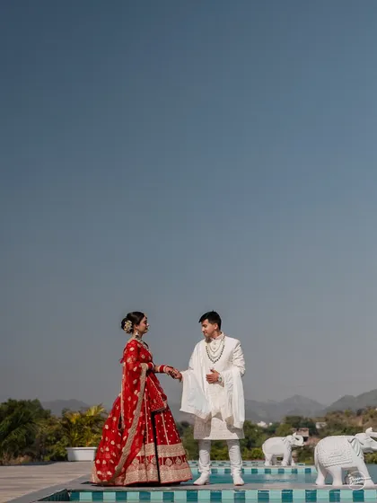 A wide shot of the couple by the pool, with the vast blue sky and hills of Udaipur creating a stunning backdrop.