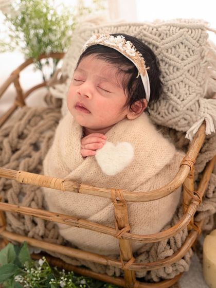 This close-up from a boho-themed shoot shows the baby wrapped in neutral tones with a soft heart accent, nestled in a rustic cane basket.