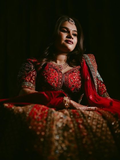 A dramatic, low-key portrait of a bride in her magnificent red lehenga. The lighting focuses solely on her, creating a regal and powerful image.