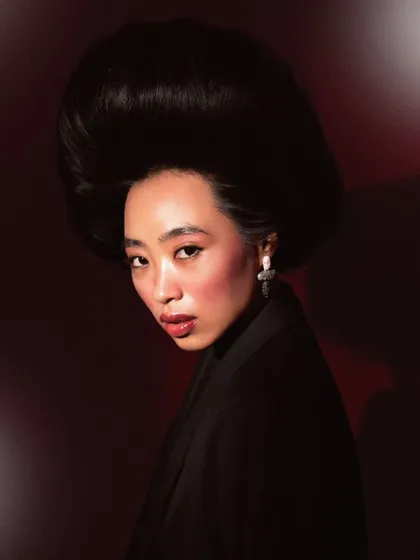 A dramatic portrait from the same series, using red-toned lighting to create a completely different mood. The model's direct gaze and the voluminous hair make for a powerful, high-fashion statement.