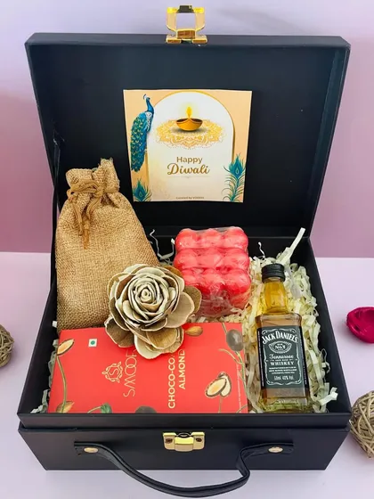 A simple yet elegant Diwali hamper in a black suitcase. It includes a miniature Jack Daniel's, a chocolate bar, a bubble candle, and a potli of nuts.