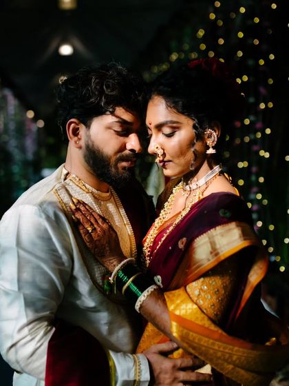 An intimate portrait of a couple in traditional Nauvari and groom's attire, set against a backdrop of festive lights. This cinematic shot highlights their close bond.