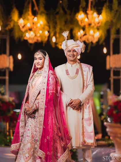 A classic wedding portrait of the couple standing together under the warm glow of chandeliers. Their elegant attire and poised smiles create a timeless and graceful image of their wedding day.