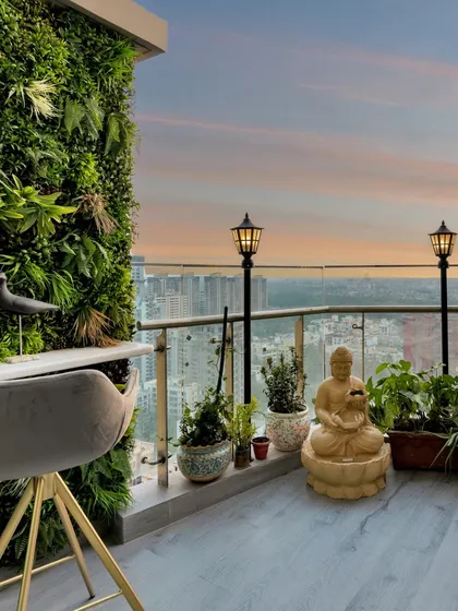 This balcony is a green paradise with a vertical garden wall. A high-top table and chair provide a perfect spot for morning coffee, while a Buddha statue adds a sense of tranquility against the city skyline.