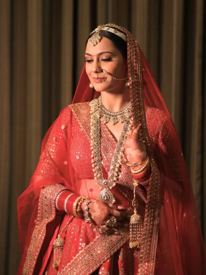 This bride looks serene and beautiful. Her makeup is soft and timeless, designed to complement her intricate jewelry and red lehenga without overpowering her features.