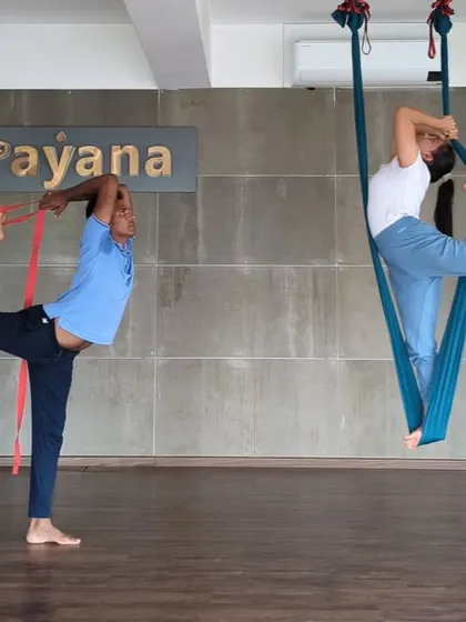 A student practices Natarajasana, using a strap for support on the mat while another explores the pose in an aerial hammock. We believe in using props to practice mindfully.