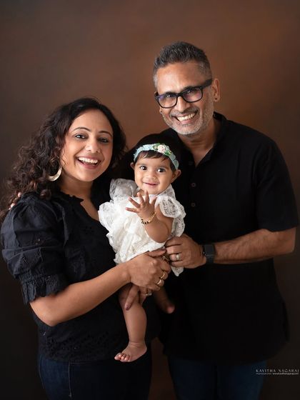 A happy family portrait with their eight-month-old daughter. Her joyful wave and her parents' smiles capture a moment of pure, uncomplicated happiness.