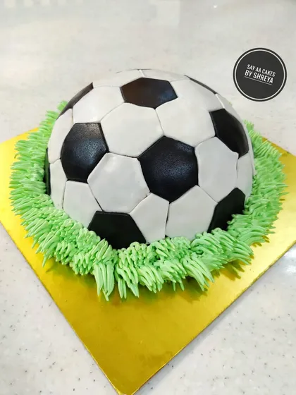 A goal-worthy celebration cake for a football fan. This 3D soccer ball is perfectly spherical and sits on a bed of green buttercream grass. Each panel is individually cut and placed for a realistic finish.
