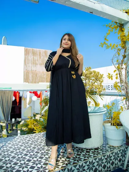 A full-length portrait on a sunny rooftop. The classic black anarkali stands out beautifully against the bright blue sky, creating a fresh and modern look for this ethnic wear shoot.