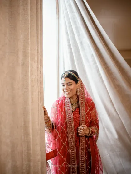 The bride looks out the window with a gentle smile, a quiet moment of anticipation before her Nikah ceremony.