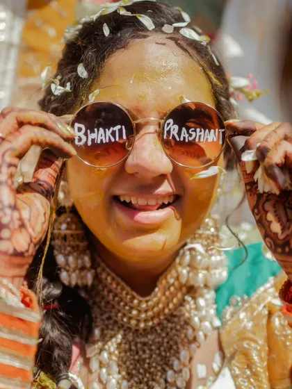 A fun and quirky Haldi portrait. The bride shows off her custom sunglasses, a playful detail that reflects her personality and adds a unique touch to the photos.