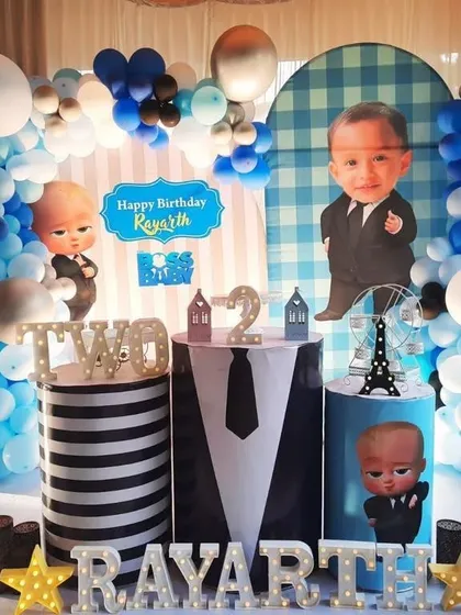 A fun Boss Baby theme with a custom backdrop featuring a caricature of the birthday boy. The decoration uses a blue, black, and white color scheme with themed pedestals.