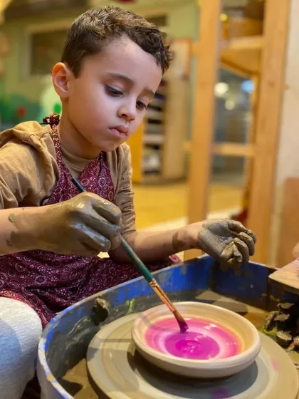 A young artist carefully paints his finished bowl. The final step of adding color allows for another layer of personalization and creative expression.