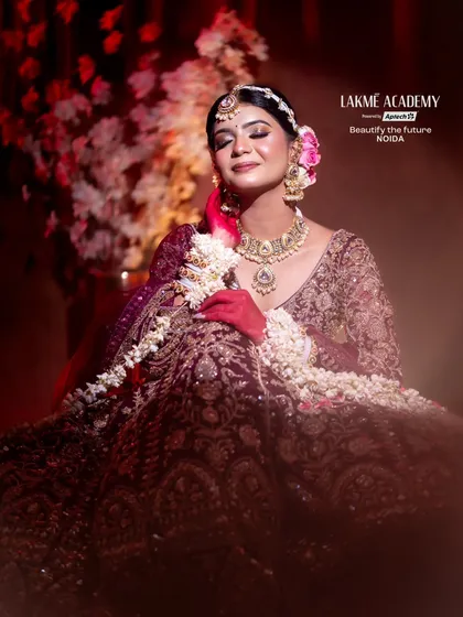 A full view of a contemporary bridal creation. The rich wine-colored lehenga is complemented by soft, glowing makeup and floral hair accessories, showcasing a complete look from our student portfolio.