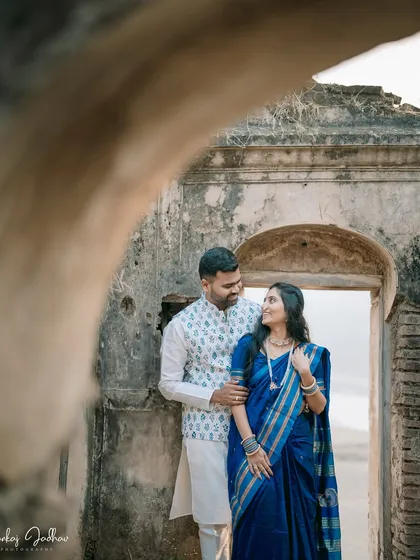 Peeking through a stone archway, we see Ankush and Aishwarya sharing a quiet moment. This creative framing adds depth and a sense of discovery to their pre-wedding portrait in Satara.