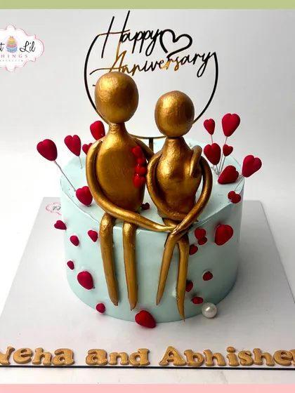 A modern and artistic anniversary cake. This design features abstract golden figures of a couple, surrounded by floating red hearts.