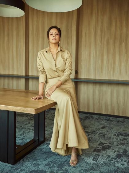 A full-length seated portrait in the beige shirt-dress, exuding quiet confidence and grace.