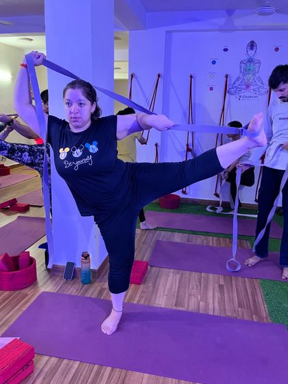 A student uses a resistance band to work on her standing split, improving both balance and flexibility.