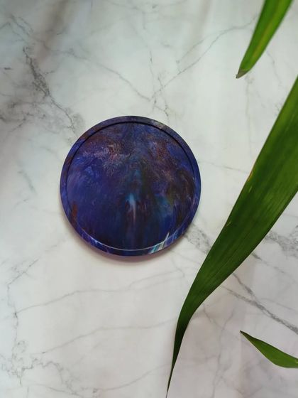 This coaster has a deep, galaxy-like pattern of blues and purples. It's a small piece of art for your tabletop, handcrafted from 100% recycled plastic.