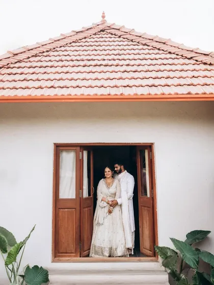 Sushma and Rohan framed in the doorway of a rustic, charming villa. The clean white walls and terracotta roof create a simple yet beautiful composition.