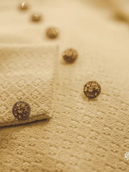 A macro shot of the custom-made jeweled buttons on the wedding sherwani. These small details are what elevate a garment from simply clothing to a cherished heirloom.