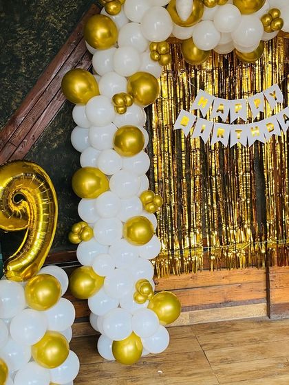 A 19th birthday party with a white and gold theme, featuring a balloon arch and foil number balloons.