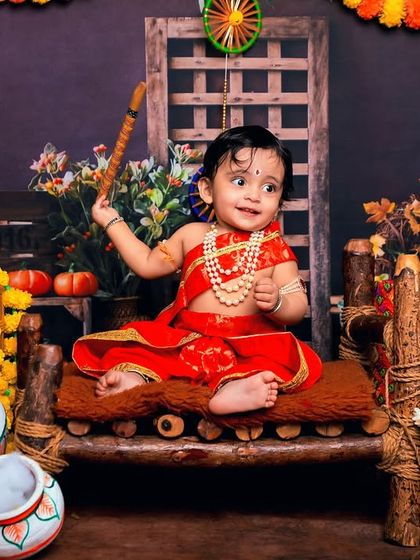 Another beautiful take on our little Krishna theme, this time with a baby girl in a lovely red costume. The setup is rich with traditional elements like makhan pots and marigolds.