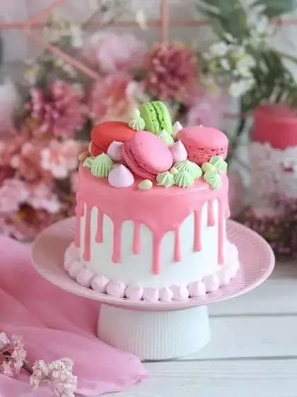 Pretty in pink! This adorable drip cake is topped with colorful macarons and meringue kisses, making it a perfect centerpiece for a sweet and stylish birthday party.