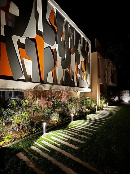The interplay of the landscape lighting with the illuminated architectural facade creates a powerful dialogue between the building and its natural surroundings.
