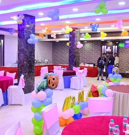 A full view of a banquet hall decorated for a birthday party. You can see the guest tables, ceiling balloons, and the main cake table area.