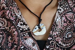 A unique, open-circle ceramic pendant with touches of gold, hanging on a black cord. It's a perfect example of modern ceramic jewelry.