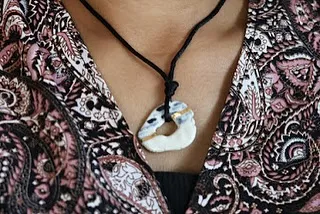 A unique, open-circle ceramic pendant with touches of gold, hanging on a black cord. It's a perfect example of modern ceramic jewelry.