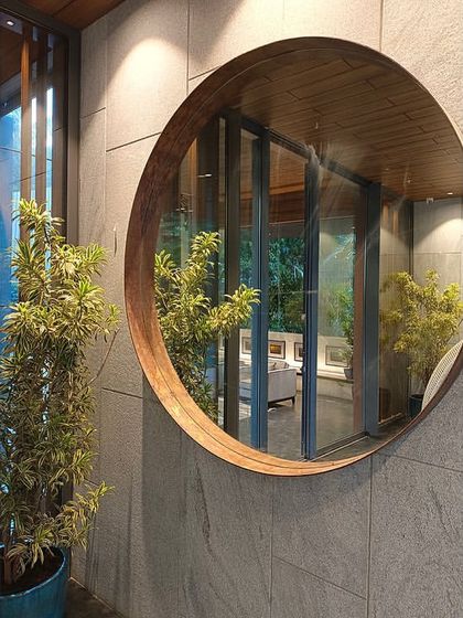 A large, wood-framed circular mirror hangs in the space between the pool and lounge, reflecting the greenery and blurring the line between inside and out.