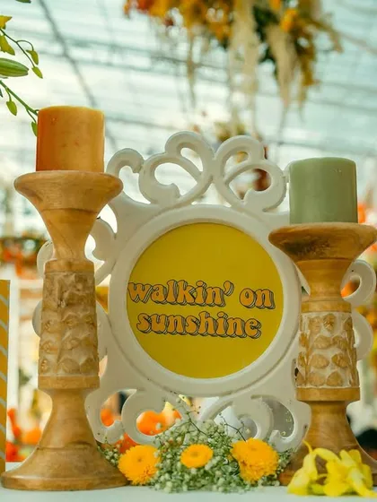 A charming detail from a 'Walkin' on Sunshine' themed brunch. The decor includes yellow-themed signage, colorful candles, and vintage books, creating a happy and whimsical tablescape.