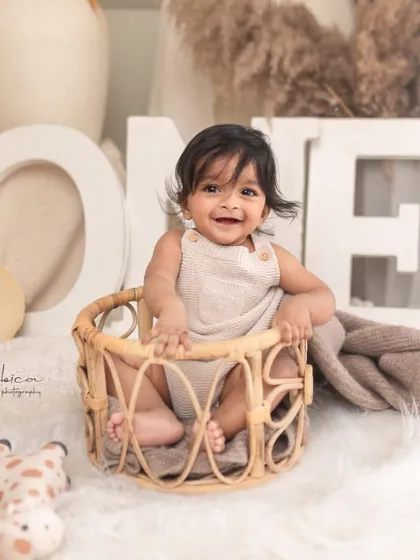 This happy baby is celebrating his first year. The 'ONE' sign and simple, neutral props keep the focus on his infectious smile and bright eyes.