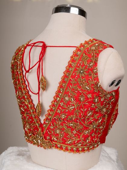 This sleeveless red blouse is perfect for a bold bridal statement. It features a deep V-neckline and is heavily embellished with intricate gold floral zardozi work, creating a rich and luxurious feel.
